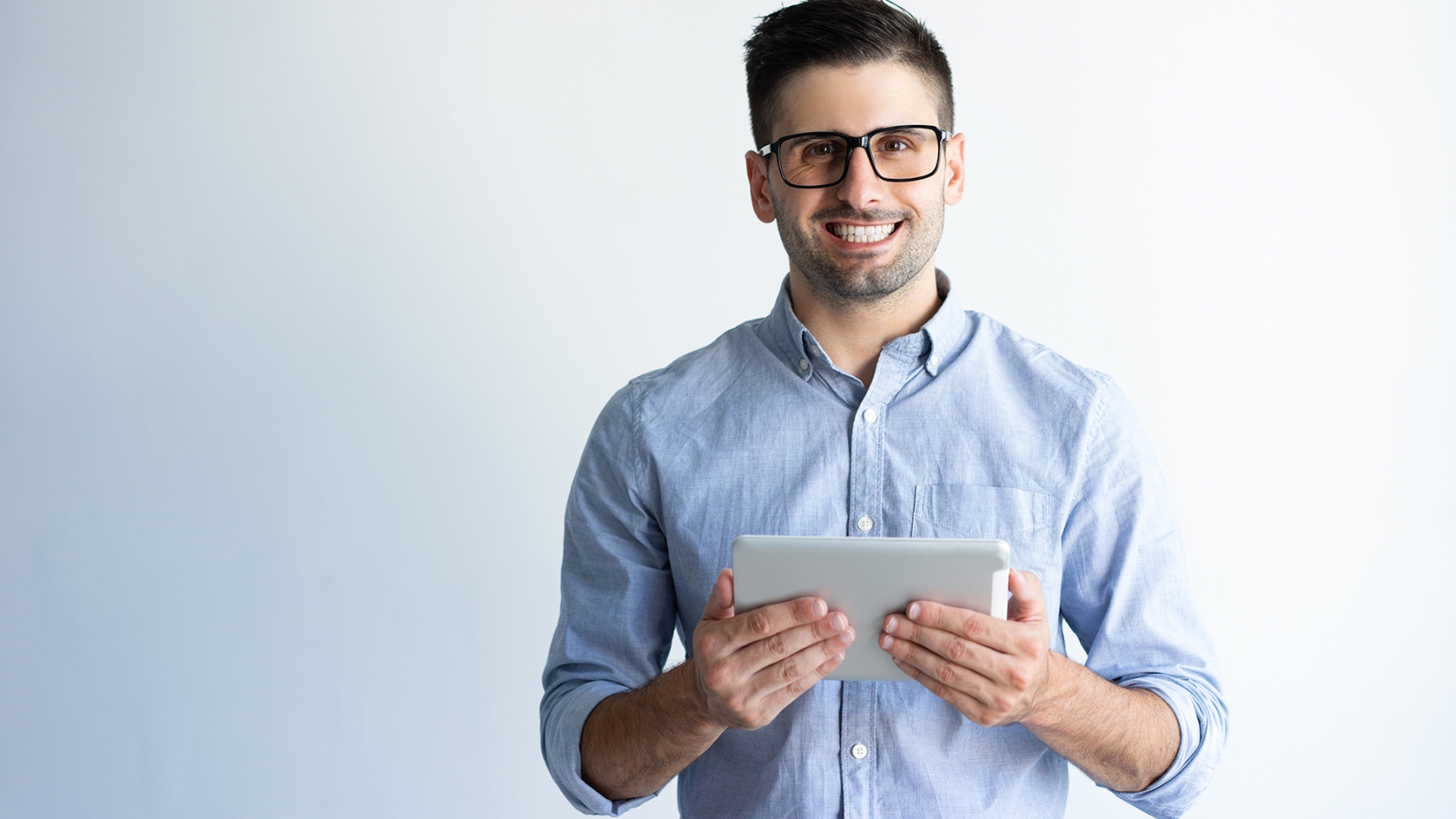 Portrait of cheerful excited tablet user wearing eyeglasses. Young Caucasian man in casual holding tablet and smiling at camera. Mobile internet concept